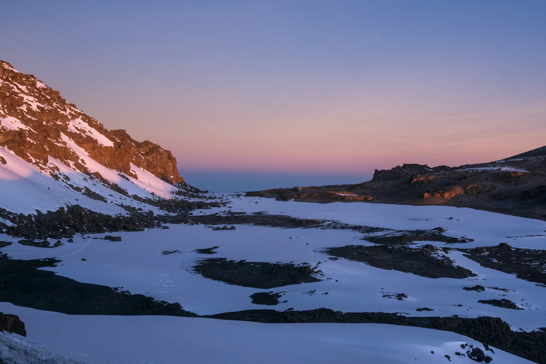 Early morning light across snow, ice and volcanic rock near the summit of Mount Kilimanjaro.